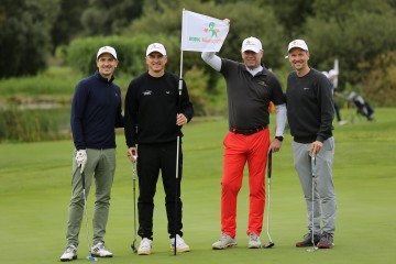 Vier Männer posieren an einem Golf-Loch 