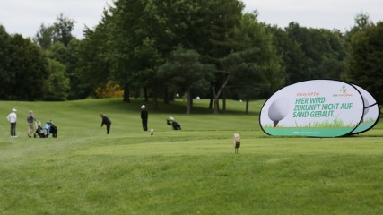 Ein Golfplatz mit einem Werbebanner im Vordergrund und spielern weiter hinten