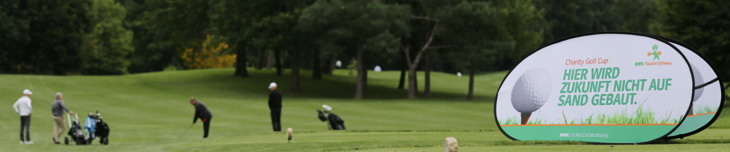 Ein Golfplatz mit Werbebanner im Vordergrund und Menschen im Hintergrund